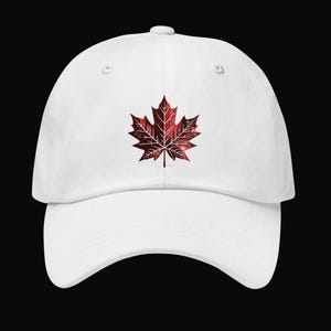 Op de afbeelding: Witte baseballcap met een rood en bordeauxkleurig esdoornblad-embleem. De cap heeft een gebogen klep en een verstelbare band. Het esdoornbladontwerp is een prominent kenmerk tegen de witte achtergrond.