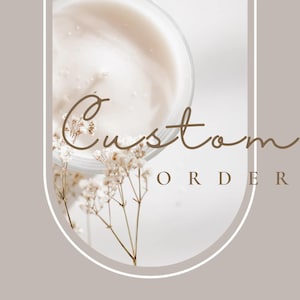 May include: A white background with a white oval frame. Inside the frame is a close-up of a clear glass jar with a white cream inside. The jar is partially obscured by a sprig of white flowers. The text "Custom Order" is written in brown cursive letters below the jar.