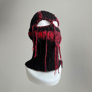 May include: Black knitted balaclava with red fringe detail. The balaclava has a cut-out for the eyes.