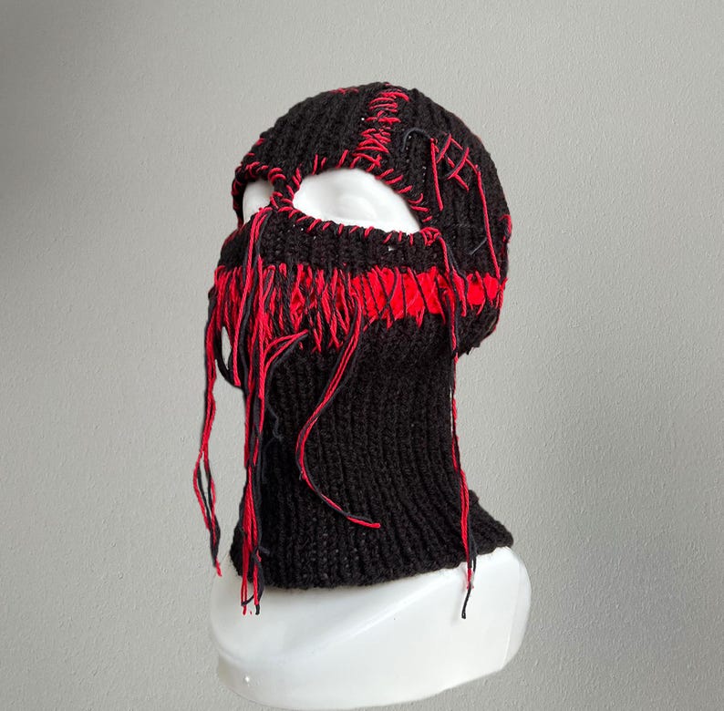 May include: Black knitted balaclava with red stitching and frayed edges. The balaclava has a hole for the eyes and nose.