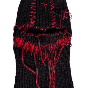 May include: Black knitted balaclava with red stitching and frayed edges. The balaclava has a hole for the eyes and nose.