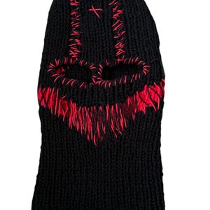 May include: Black knitted balaclava with a red skull design. The skull is outlined in red yarn and has two eye holes.