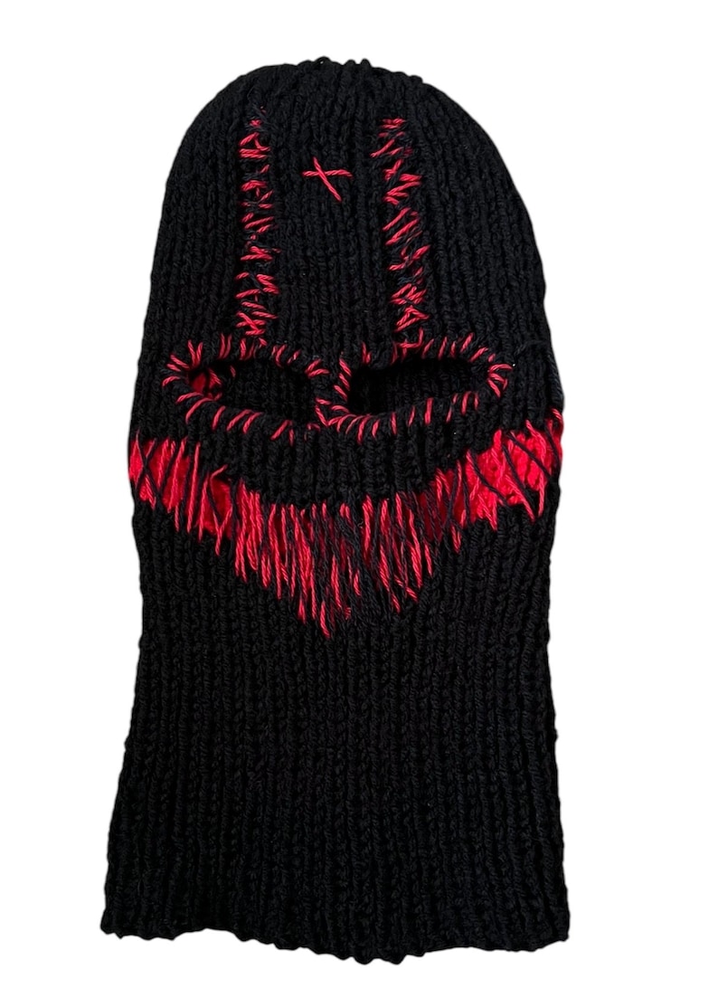 May include: Black knitted balaclava with a red skull design. The skull is outlined in red yarn and has two eye holes.