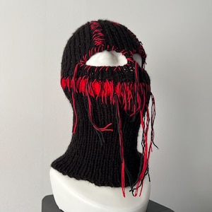 May include: Black knitted balaclava with red stitching and frayed edges. The balaclava has a hole for the eyes and nose.