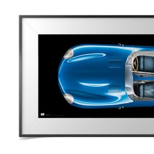 Pode incluir: Impressão emoldurada de um carro esportivo azul clássico, visto de cima, em um fundo preto. O carro tem detalhes prateados, incluindo faróis e acabamentos. O interior é visível, com um volante de madeira e assentos azuis.
