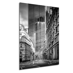 May include: A black and white photograph of a narrow street in a city with tall buildings on either side. The buildings are modern and have many windows. The street is empty and there are no people in the photo.