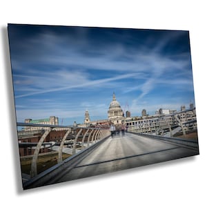Puede incluir: Fotografía del Puente del Milenio en Londres, con la Catedral de San Pablo al fondo. El cielo es azul con vetas de nubes. Las personas aparecen borrosas mientras cruzan el puente.