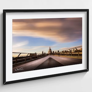 Può includere: Fotografia incorniciata del Millennium Bridge a Londra, con la Cattedrale di St. Paul sullo sfondo. Il cielo mostra una miscela di tonalità blu, arancioni e rosa. Sono visibili le ringhiere metalliche e la passerella del ponte.