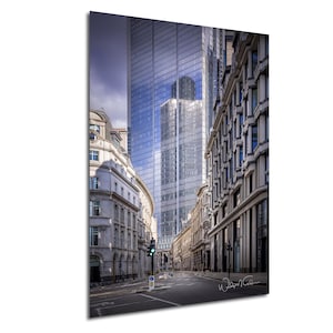 May include: A view down a narrow street in London, England. Tall modern office buildings line the street, with older buildings on either side. The street is empty, with a green traffic light at the end of the street.