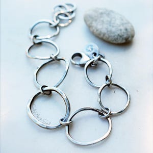 K&ouml;nnte beinhalten: Ein silberfarbenes Kettenarmband bestehend aus mehreren unregelm&auml;&szlig;igen, handgeh&auml;mmerten kreisf&ouml;rmigen Gliedern unterschiedlicher Gr&ouml;&szlig;e. Das Armband verf&uuml;gt &uuml;ber einen Karabinerverschluss und einen kleinen runden Anh&auml;nger mit Sternengravur. Der Text Art & Soul ist sichtbar.