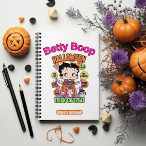 以下が含まれることがあります： 白い表紙にベティ・ブープのハロウィーンのデザインが施された、スパイラル綴じのノート。表紙には「Betty Boop Halloween」と「Trick or Treat」と書かれています。画像には、カボチャ、ペン、その他のハロウィーンをテーマにした装飾が含まれています。