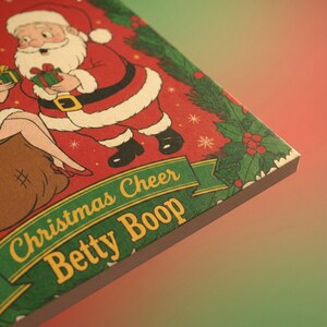 May include: A Christmas-themed illustration featuring Santa Claus and Betty Boop on a red background. The text "Christmas Cheer Betty Boop" is displayed on a green banner. The image has a festive holiday theme.
