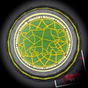 May include: Circular coaster with a geometric bear design in green and yellow. The coaster has a black edge with yellow and green accents, and a gray border. The design is centered on a black background.