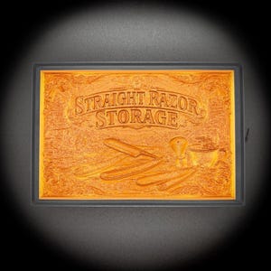 Peut inclure: Plaque rectangulaire en bois teinté orange avec l'inscription "STRAIGHT RAZOR STORAGE" gravée. La plaque présente des images gravées de rasoirs droits, d'un blaireau et d'une tasse. La plaque est encadrée de noir.