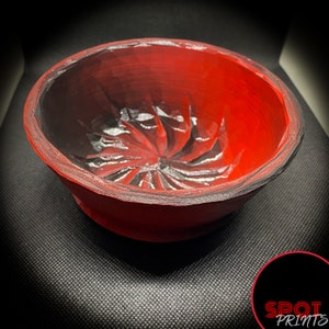 Puede incluir: Un cuenco de cerámica rojo y negro con un diseño de espiral en el centro. El cuenco está hecho a mano y tiene un acabado brillante.