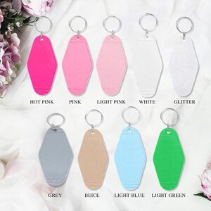K&ouml;nnte beinhalten: Eine Auswahl an Schl&uuml;sselanh&auml;ngern im Motel-Stil in verschiedenen Farben: Pink, Hellrosa, Wei&szlig;, Glitzer, Grau, Beige, Hellblau und Hellgr&uuml;n. Jeder Schl&uuml;sselanh&auml;nger hat einen silbernen Ring.