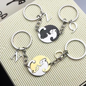 Könnte beinhalten: Schlüsselanhänger mit silbernen Ringen, Ketten und Anhängern. Die Anhänger zeigen ein Yin-Yang-Design mit Katzen in Schwarz und Weiß sowie Gold und Weiß. Einzelne Schlüsselanhänger haben die Buchstaben "Z", "9" und "N".