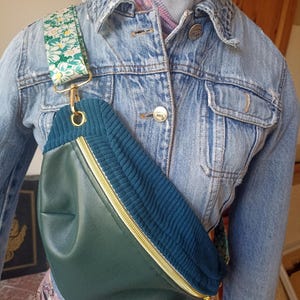 Könnte beinhalten: Eine grüne Gürteltasche aus Kunstleder und blauem Cord mit goldenem Reißverschluss und einem floralen Riemen.