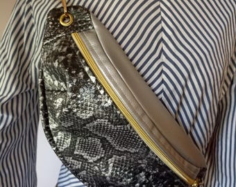 May include: A black and silver snakeskin patterned fanny pack with a gold zipper and red strap.