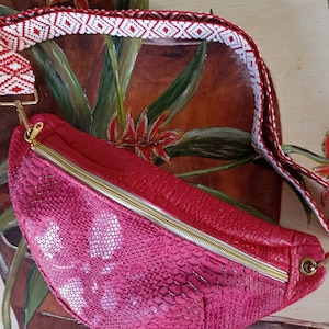 Peut inclure: Une banane rose en peau de serpent avec une fermeture éclair dorée et une sangle à motif rouge et blanc.