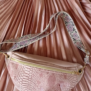 Peut inclure: Une banane rose à texture de peau de serpent avec une fermeture éclair dorée et une sangle à motif floral.