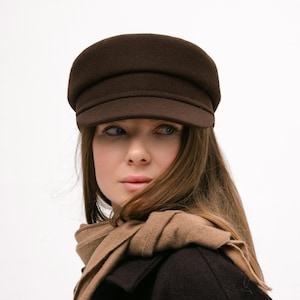 May include: A dark brown wool newsboy cap with a structured crown and a short, stiff brim. The cap features a smooth, felted texture and a horizontal band detail above the visor, providing a classic, rounded silhouette that sits firmly on the head.