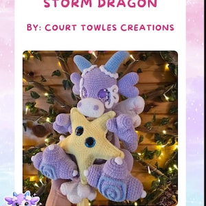 May include: A crocheted purple and light blue dragon plush toy holding a yellow star with large blue eyes. The text above reads STELLALUNA THE STORM DRAGON BY: COURT TOWLES CREATIONS. The dragon features horns, wings, and swirl patterns.