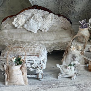 May include: Miniature bedroom set with a white lace-covered bed, a small stool, and a decorative duck on wheels. A small bag with flowers and text is also present. The scene is decorated in a vintage style.