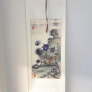 May include: A vertical wall scroll featuring a traditional ink-wash style painting of several purple and black ghost-like creatures with red eyes and wide grins. The scene depicts rocky cliffs, sparse vegetation, and a pale moon, finished with red stamps.