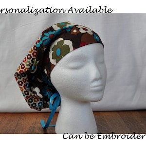 May include: A floral patterned scrub cap with brown, blue, and white flowers. The cap has a blue ribbon tie and the text "Personalization Available" and "Can be Embroidered".