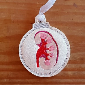 May include: White felt Christmas ornament with a red and pink embroidered kidney design.