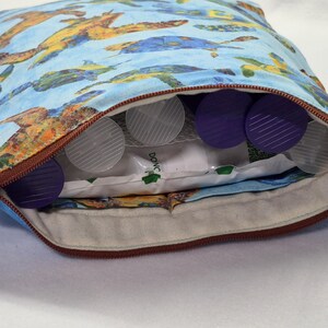 May include: A zippered pouch with a blue background and a pattern of sea turtles in shades of blue, yellow, and orange. The pouch is partially open, revealing several clear and purple plastic objects and a white package.