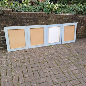 May include: Four light blue picture frames with a gold trim and a light brown backing. The frames are arranged in a row on a brick patio.