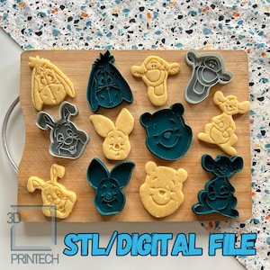 Puede incluir: Una tabla de cortar de madera muestra cortadores de galletas y galletas horneadas con forma de personajes de dibujos animados. Los cortadores son de color verde azulado, gris y amarillo. Las galletas son doradas. El texto "STL/DIGITAL FILE" es visible.
