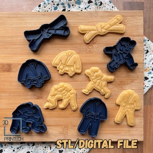 Könnte beinhalten: Eine Sammlung von Karate-Ausstechern und Keksen auf einem Holzschneidebrett. Die Ausstecher sind marineblau und die Kekse sind hellbraun, geformt wie Karate-Uniformen und -Gürtel. Der Text "STL/DIGITAL FILE" befindet sich unten.