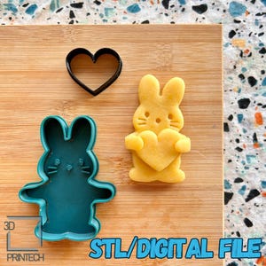 以下が含まれることがあります： ウサギがハートを持っている形、ウサギの形、ハートの形の3つのクッキー型セット。型は青と黒のプラスチック製です。画像の下部に青色のテキストでSTL/DIGITAL FILEと記載されています。