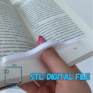 Puede incluir: Un porta páginas para libros impreso en 3D en blanco. El porta páginas está diseñado para ajustarse a un dedo y mantener la página en su lugar. El texto "STL/DIGITAL FILE" es visible en la imagen.