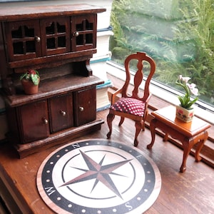 Può includere: Una piccola credenza in legno con un armadio a vetrina, un armadio inferiore con tre cassetti e un tappeto a forma di bussola sul pavimento. La credenza è decorata con una piccola pianta in vaso.