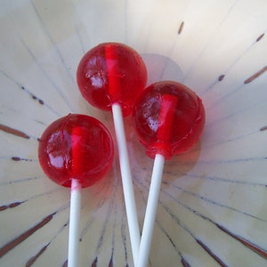 May include: Three red lollipops on a white plate with a brown and white pattern.