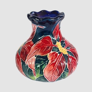May include: A ceramic vase with a round body and a ruffled rim. The vase is decorated with red poinsettia flowers and green leaves against a dark blue background. The flower's center is yellow.