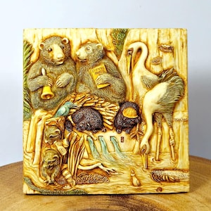 May include: A square, off-white relief sculpture featuring a forest scene with animals. Two bears, one holding a bell, are central. Other animals include a crane, hedgehogs, and raccoons. The text "Lloyds Bears" is visible on a book.