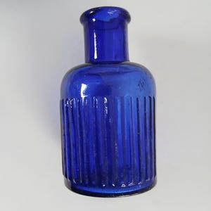 May include: A cobalt blue glass bottle with a ribbed design. The bottle has a short neck and a rounded body.