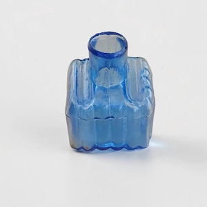 Peut inclure: Petite bouteille en verre bleu antique, base carrée et col cylindrique. La bouteille présente des rainures verticales et une surface légèrement texturée. La couleur est un bleu transparent vif, et la bouteille semble vide.