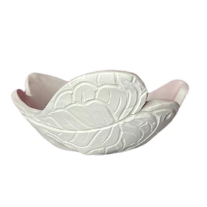 May include: A white ceramic bowl shaped like a blooming flower with overlapping petals. The exterior surface features a detailed, embossed leaf vein pattern, while the interior of the bowl reveals a smooth, pale pink finish on the curved petals.