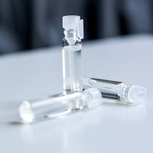 May include: Three clear glass bottles with white caps containing a liquid. The bottles are on a white surface.