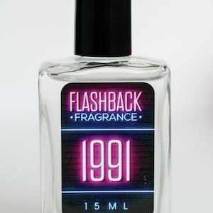 May include: A clear glass perfume bottle with a black cap. The label reads "FLASHBACK FRAGRANCE" above the year "1991" in neon pink. The bottle contains 15 ml of fragrance.