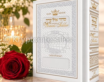 May include: A white hardcover book titled The ArtScroll Women's Siddur Klein Edition with gold foil lettering and decorative borders. The cover features a central illustration of the Western Wall, a crown icon, and the text ArtScroll Series.
