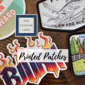Pode incluir: Uma coleção de patches bordados com vários designs, incluindo um patch "3 YEAR AWARD", um patch "Foundry" com uma ilustração de peixe e um patch com o texto "The Jeep Ra". A imagem também inclui um patch com a palavra "Printed Patches".