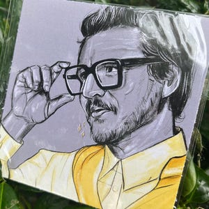Könnte beinhalten: Porträtillustration eines Mannes mit Brille, gelbem Hemd und grauem Hintergrund. Das Kunstwerk befindet sich in einer transparenten Plastikhülle, mit einer Signatur unten rechts. Das Bild ist von grünen Blättern umgeben.