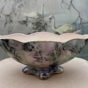 May include: A decorative ceramic bowl with an iridescent finish, scalloped rim, and pedestal base. The bowl has a pearlescent sheen with purple, green, and gold hues. The rim and base are trimmed with gold. Likely a vintage piece.
